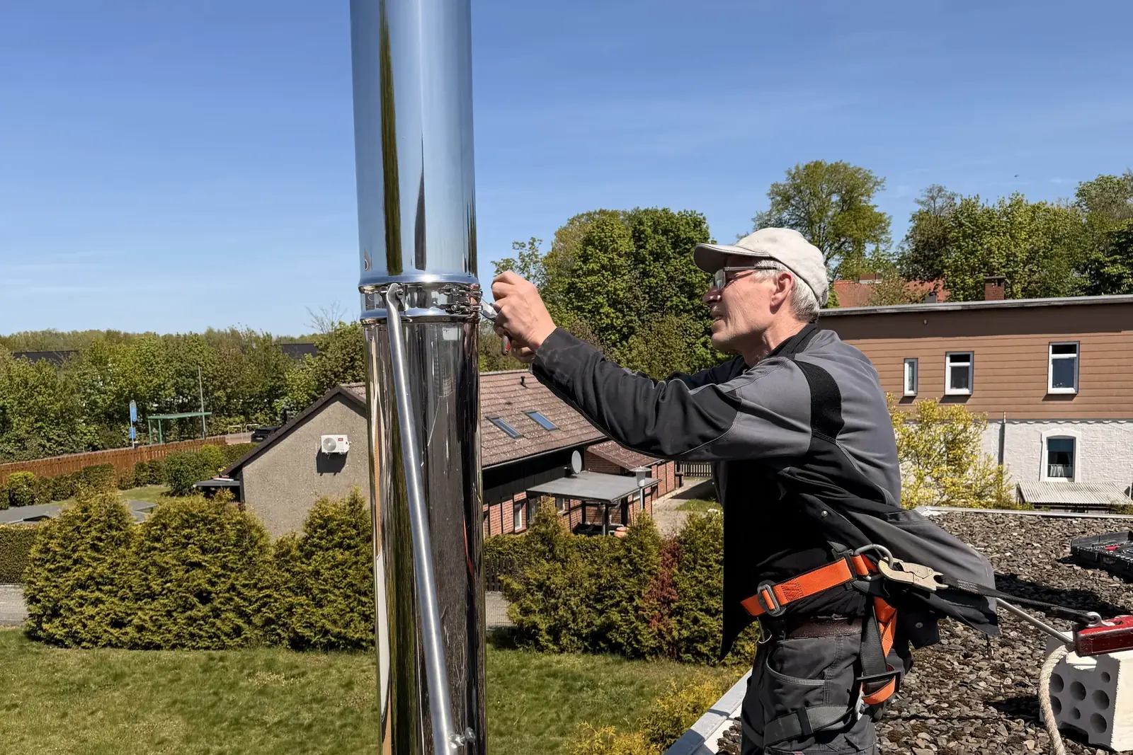 369 Vision Werk fitter wearing a safety harness installing a stainless-steel chimney, with houses in the background